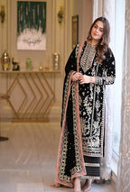 Woman in a black and white embroidered traditional outfit standing in a decorated room.