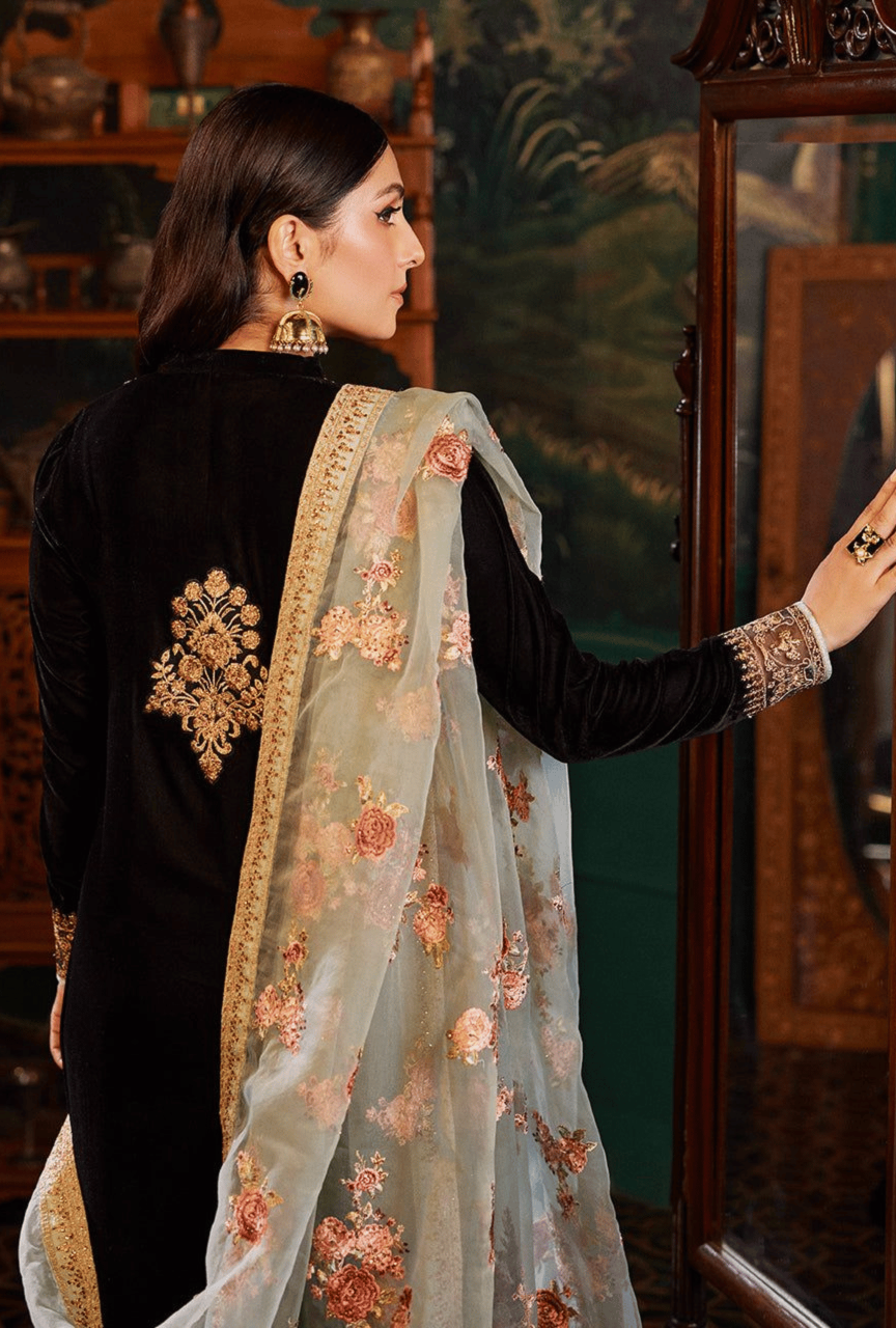 Woman wearing a black outfit with floral embroidery, standing in front of a mirror.