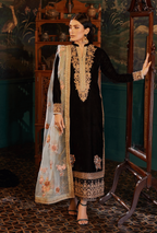 Woman in traditional black and gold embroidered outfit standing in a decorated room.
