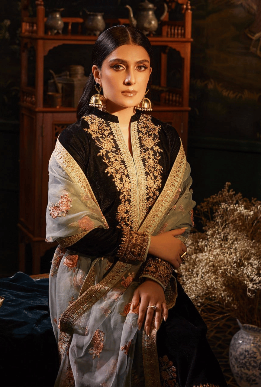 Woman in an embroidered traditional outfit sitting in a decorative setting.