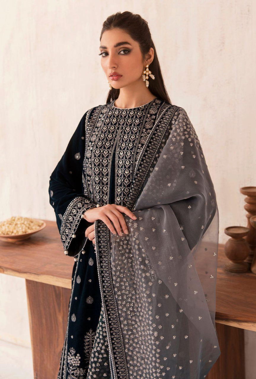 Woman wearing a black and white embroidered traditional outfit with a sheer dupatta in a minimalistic setting.