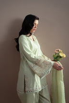 Woman in a light green traditional outfit holding flowers against a plain background