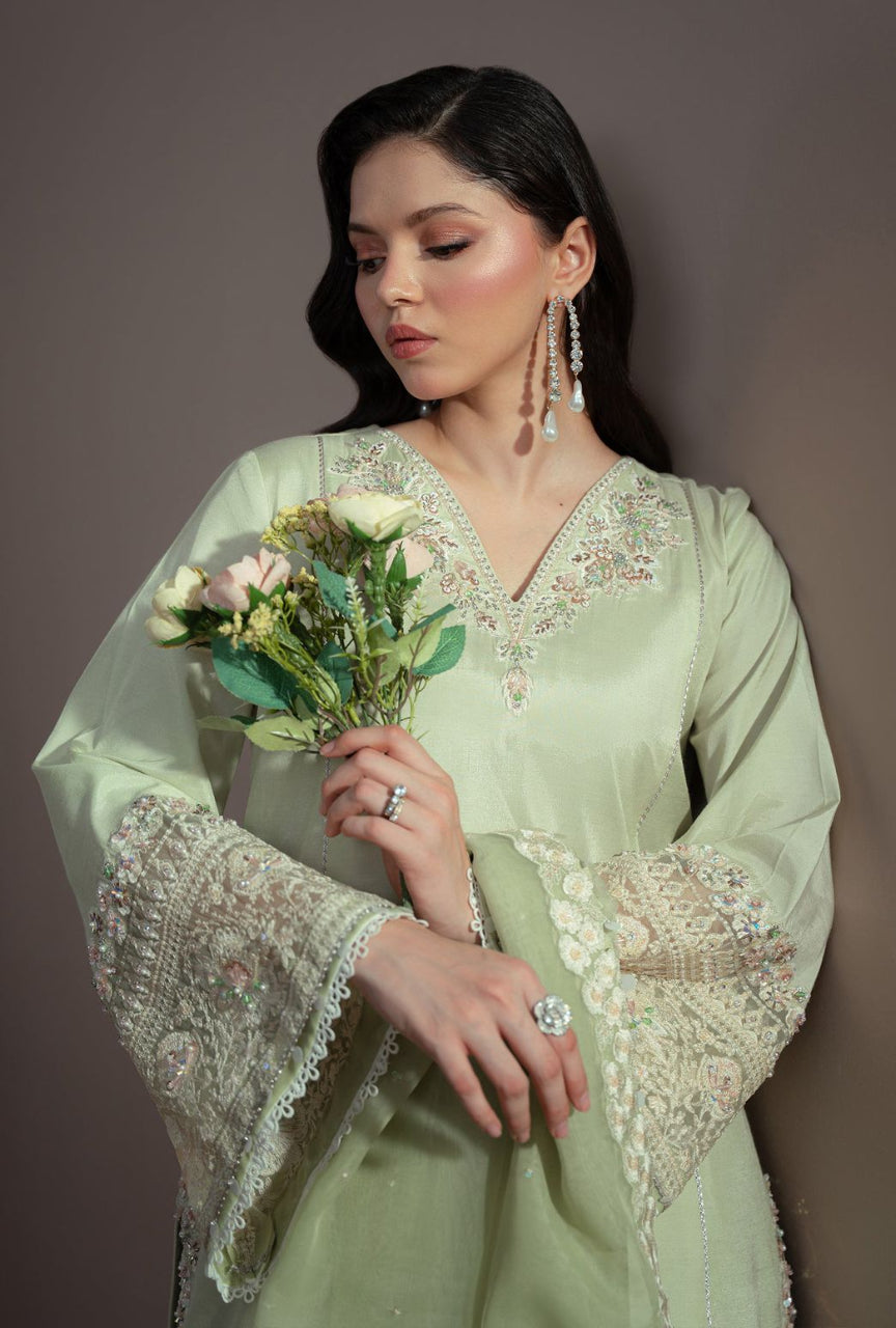 Woman in a light green embroidered outfit holding flowers against a plain background