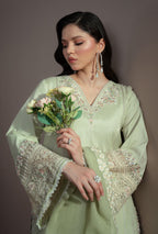 Woman in a light green embroidered outfit holding flowers against a plain background