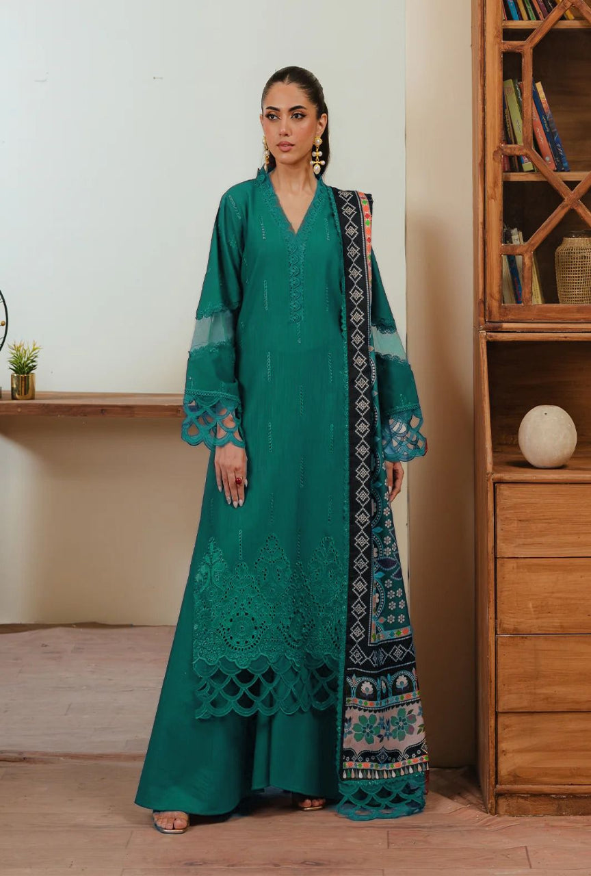 Woman wearing a teal embroidered outfit standing in a room with wooden furniture.