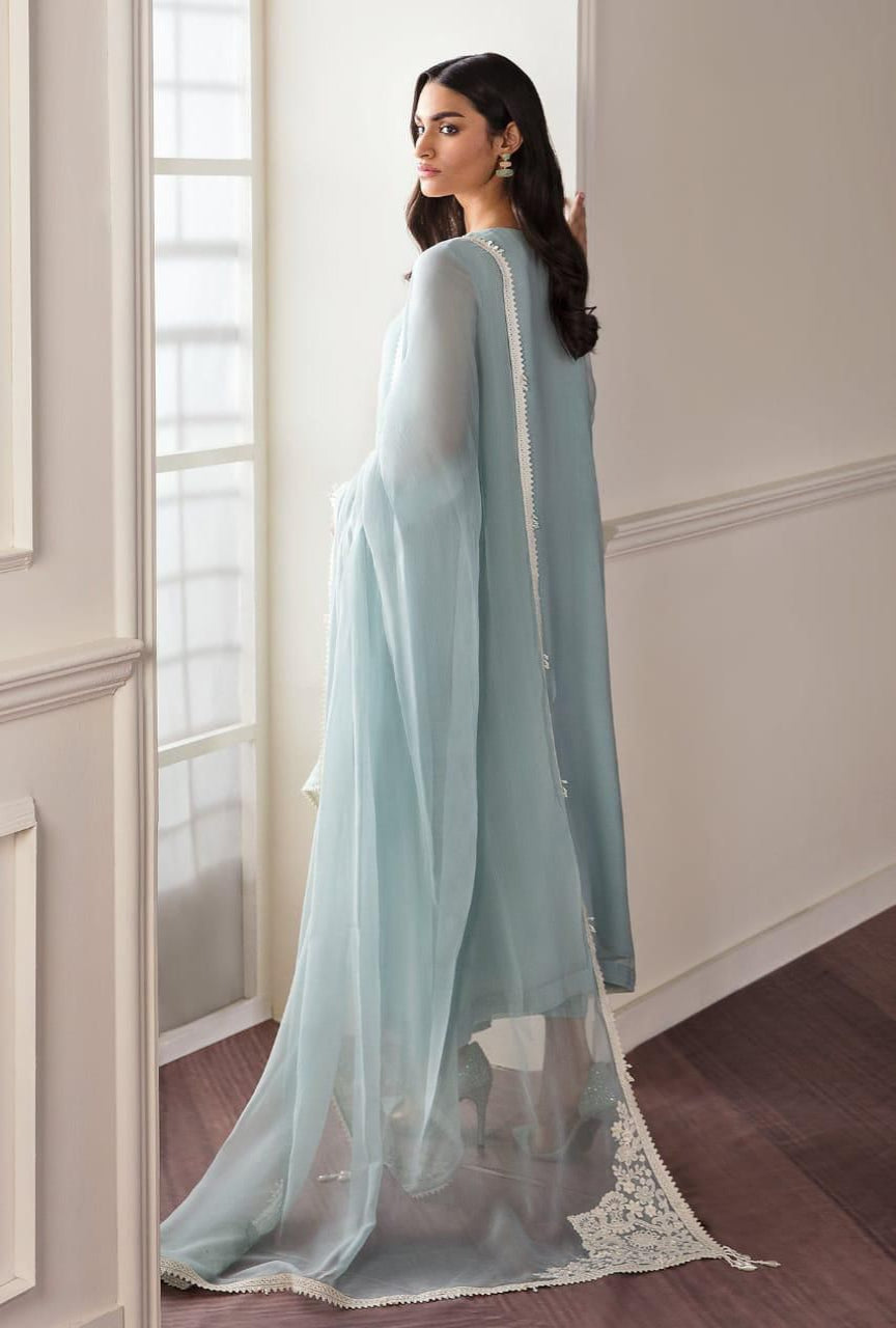 Woman wearing a light blue traditional outfit with a sheer dupatta in a room with white walls and wooden floor.