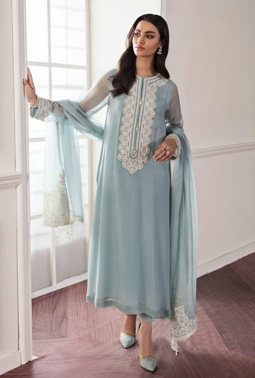 Woman wearing a light blue traditional outfit with lace details in a room.