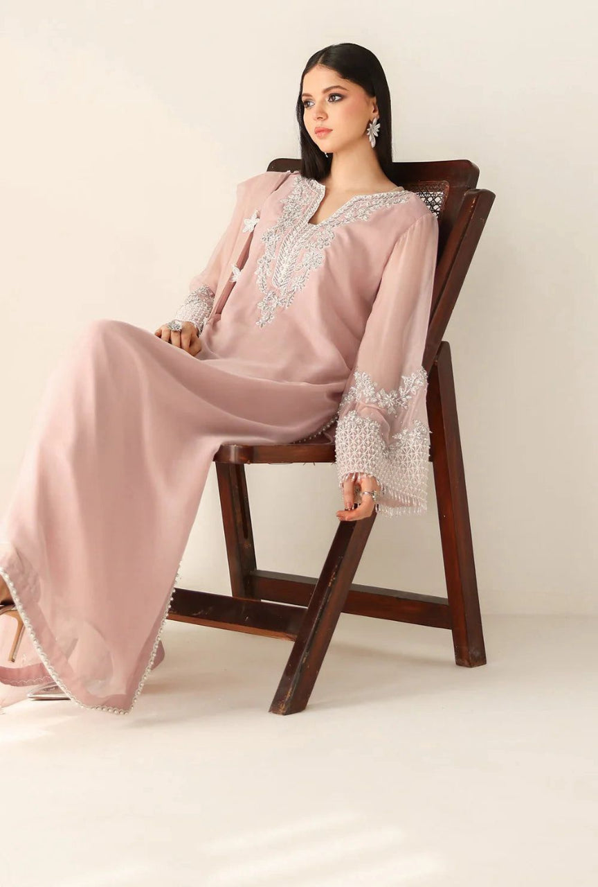 Woman in a pink traditional outfit with silver embroidery sitting on a wooden chair against a white background