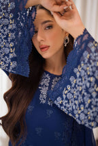 Woman wearing a blue embroidered dress with a matching headscarf.