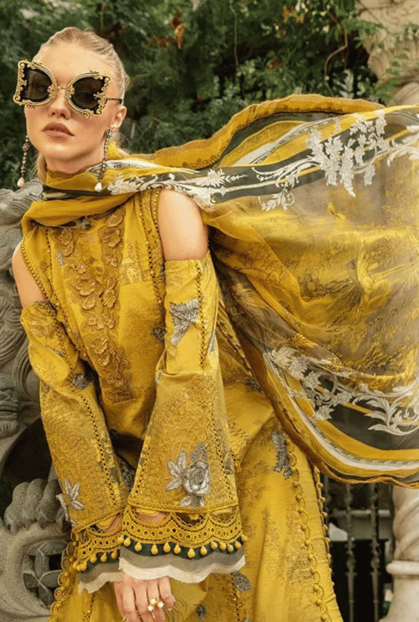 Person wearing a yellow embroidered outfit with a large sheer scarf, standing outdoors.
