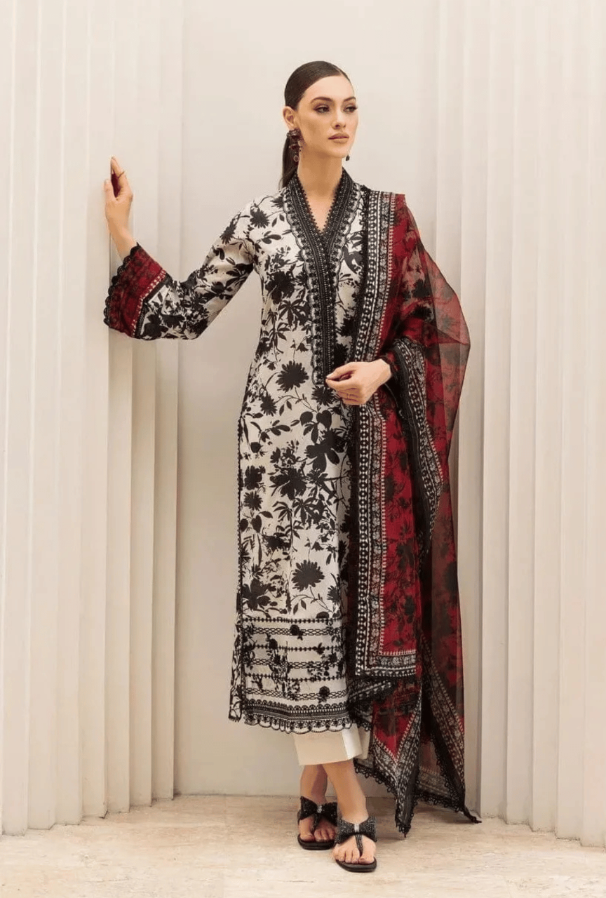 Woman wearing a floral dress with a red and black patterned dupatta against a white curtain background