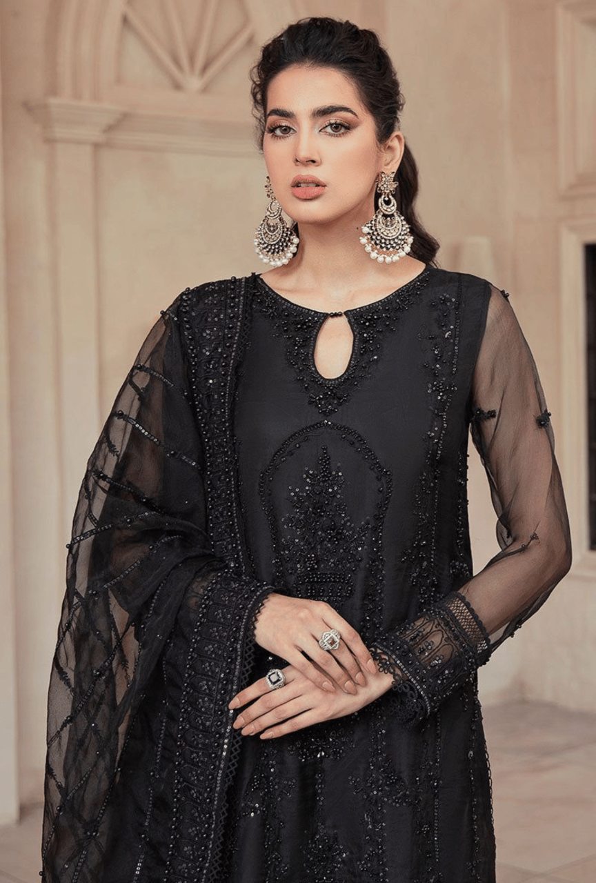 Woman wearing a black embroidered outfit with sheer sleeves and a matching shawl indoors.