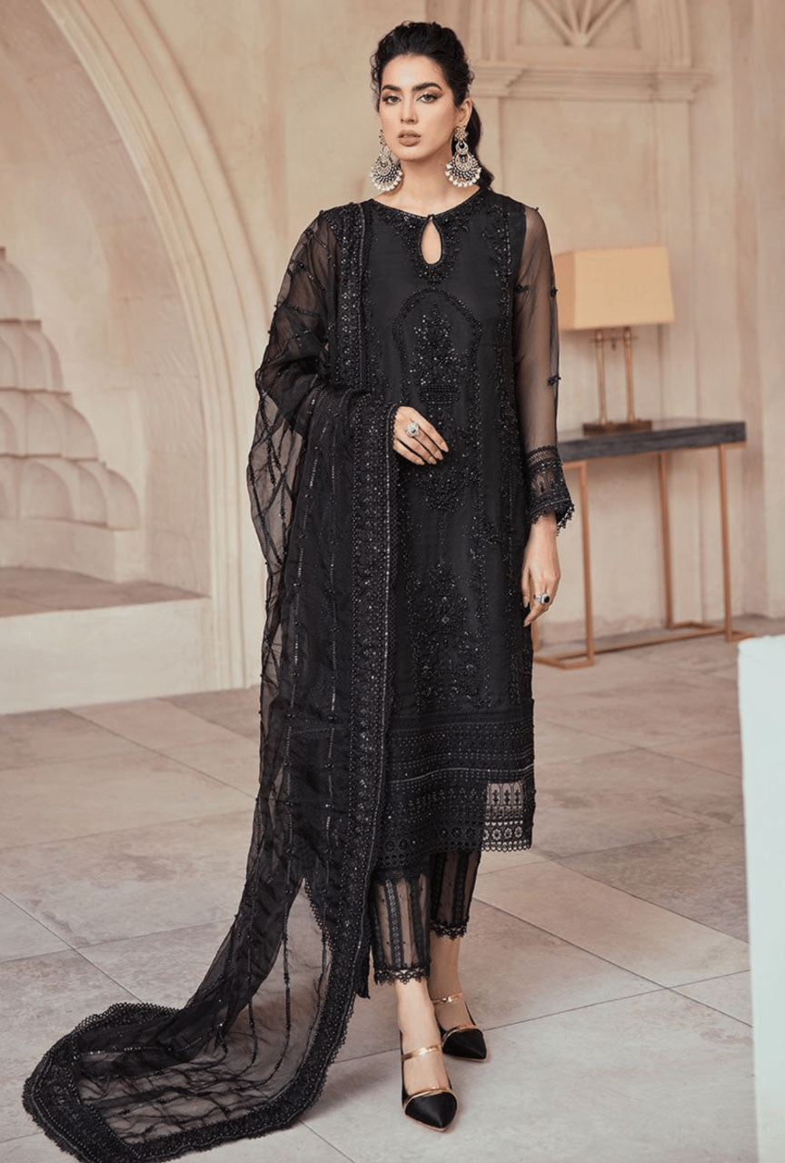 Woman wearing a black embroidered outfit with a long scarf in an elegant interior setting.