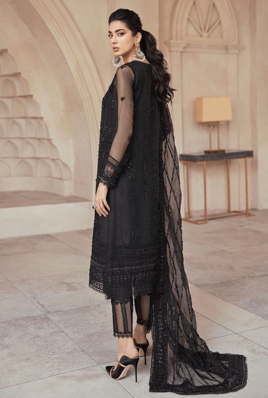 Woman in a black embroidered outfit standing in an elegant interior setting.