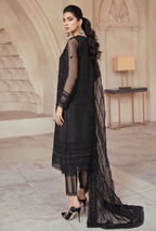 Woman in a black embroidered outfit standing in an elegant interior setting.