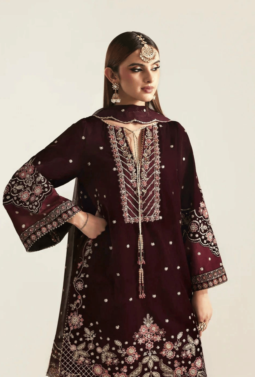 Woman wearing a maroon embroidered traditional outfit with intricate designs on a plain background