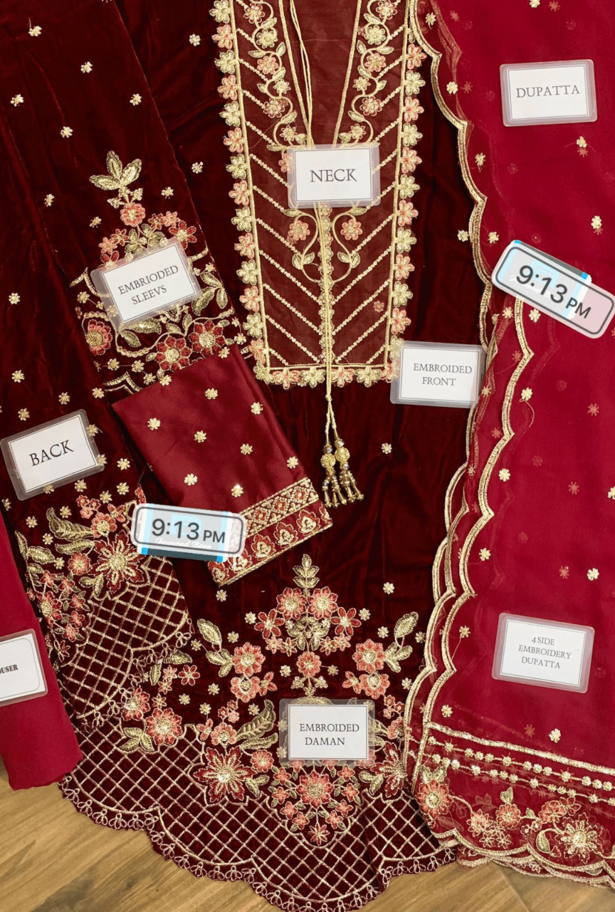 Red embroidered garment with labels indicating different parts and times, on a wooden surface.