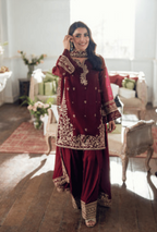 Woman in a red traditional outfit with gold embroidery in a decorated room.