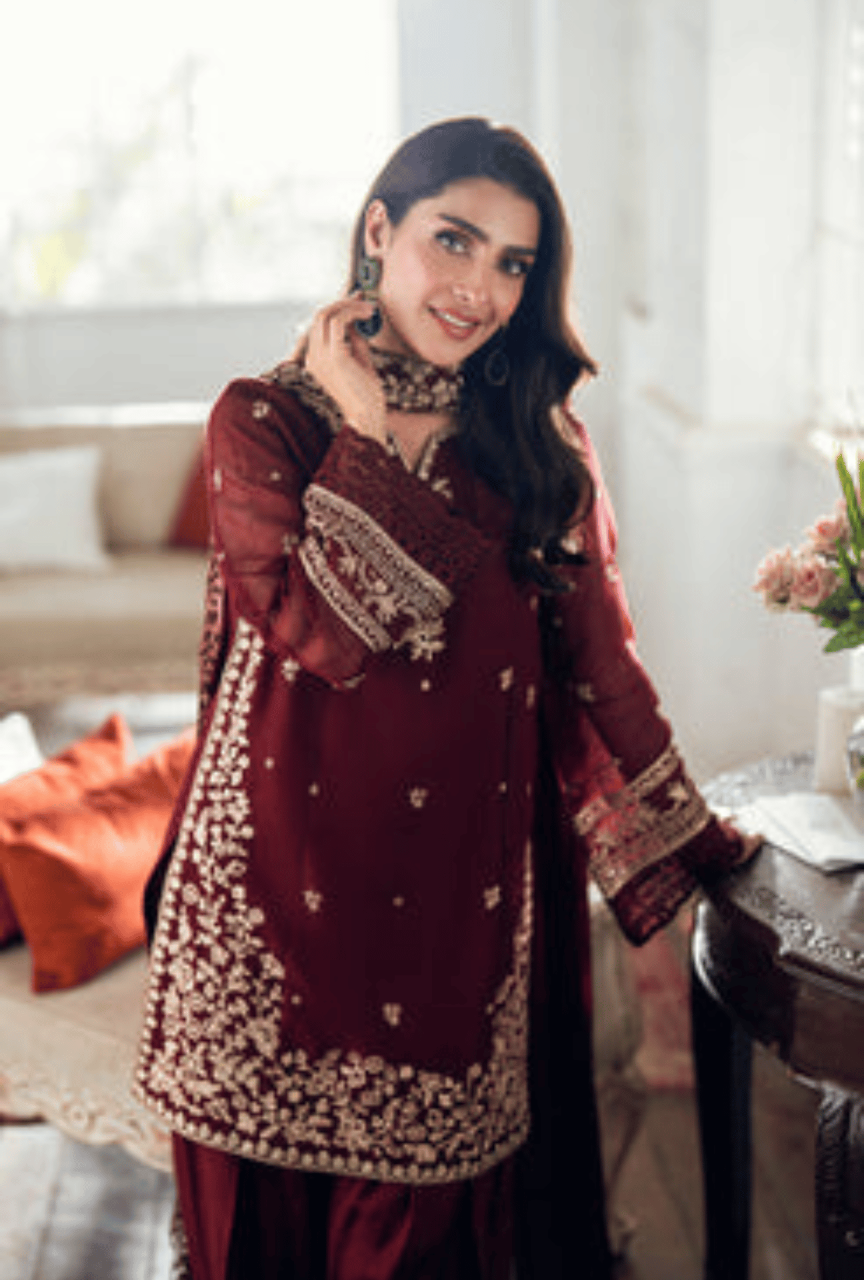 Woman in a maroon traditional outfit with gold embroidery in a bright room.