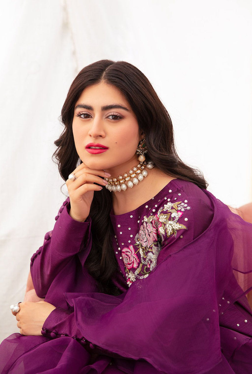 Woman wearing a purple traditional outfit with floral embroidery on a white background