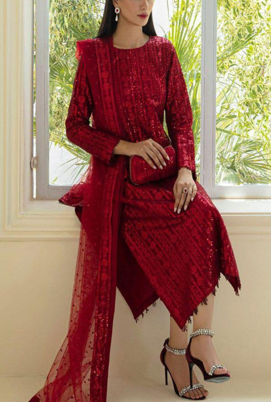 Woman in a red traditional outfit with a matching dupatta, standing in front of a window with greenery outside.