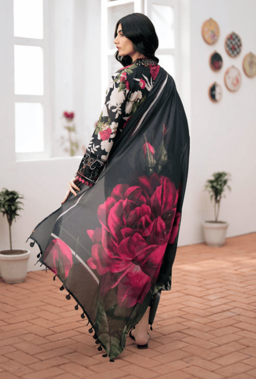 Woman holding a black floral scarf with red roses in a room with plants and decorative plates on the wall.