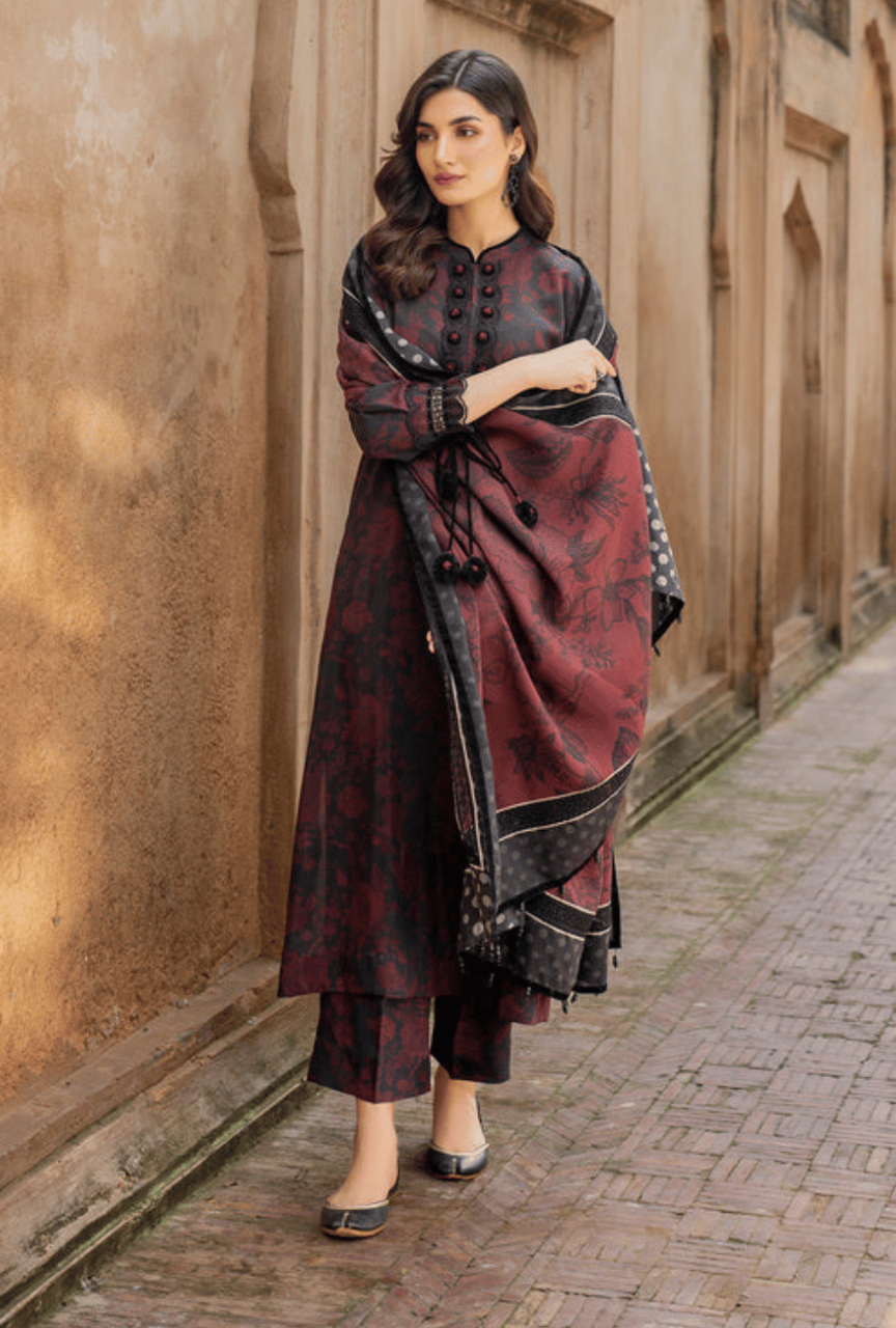 Woman in a traditional maroon and black outfit standing against a stone wall.