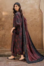 Woman wearing a dark red and black traditional outfit with a long scarf against a stone wall.