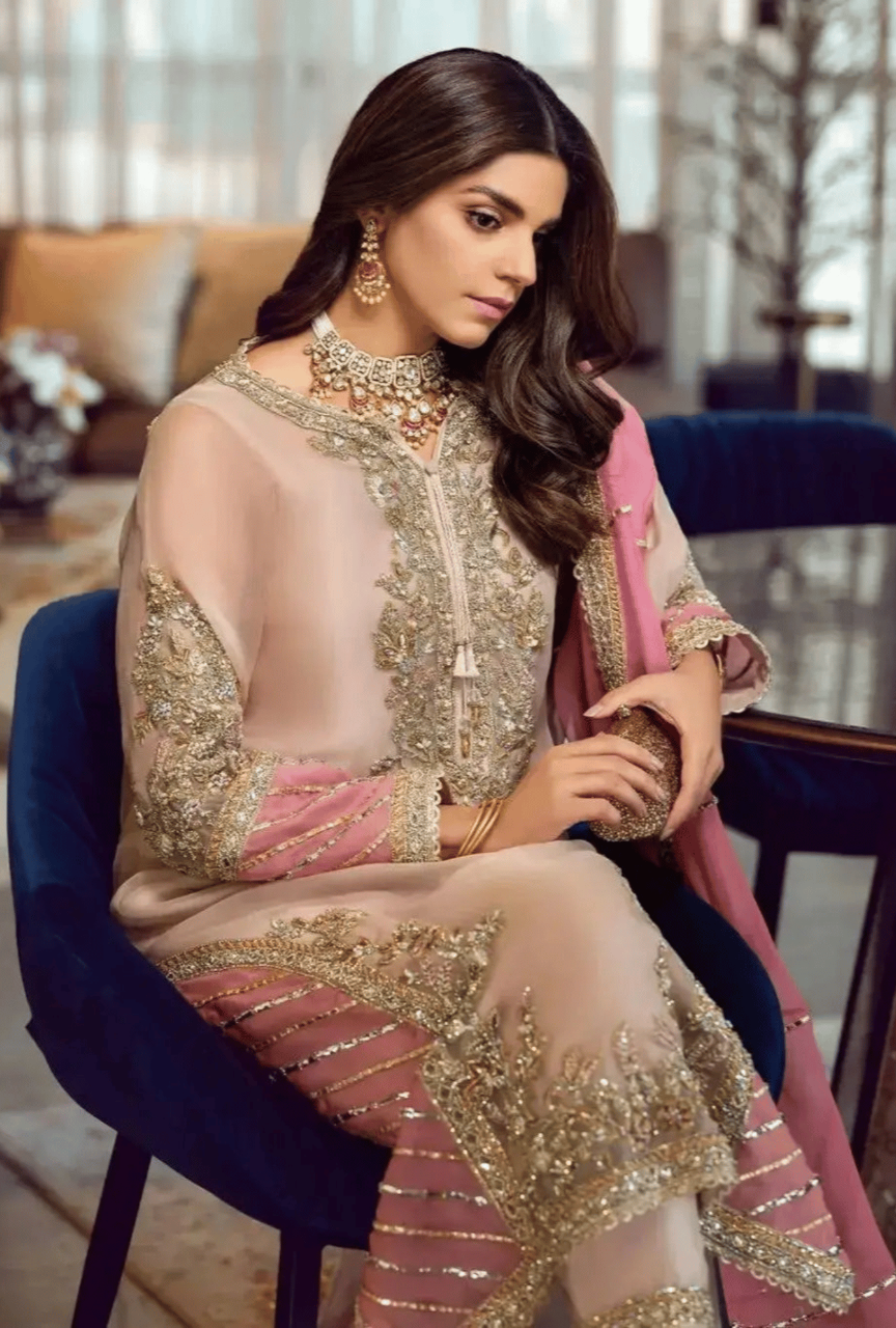 Woman in a traditional embroidered outfit sitting on a chair indoors.