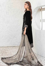 Woman in a black traditional outfit with a long, flowing scarf against a white wall.