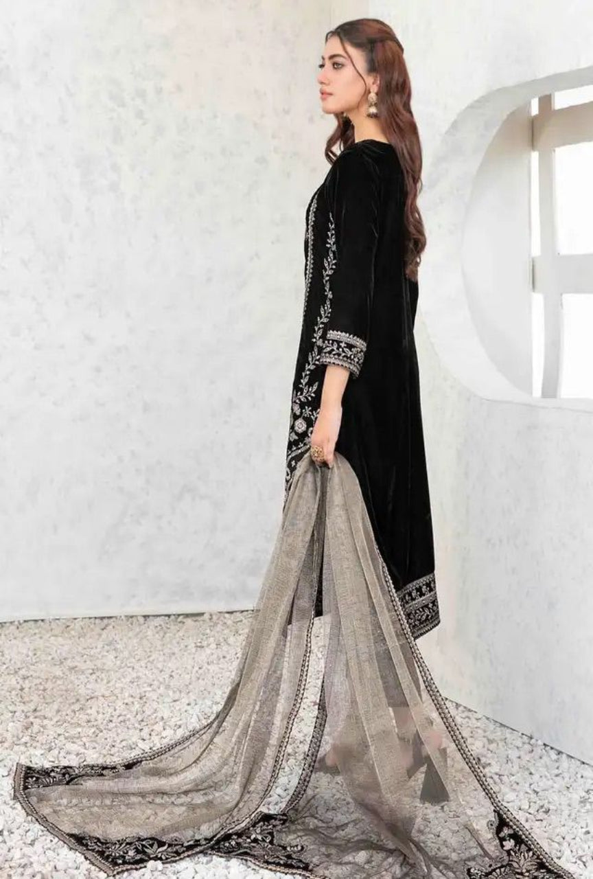 Woman in a black traditional outfit with a long, flowing scarf against a white wall.