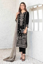 Woman wearing a black embroidered outfit with a sheer dupatta in a minimalistic setting