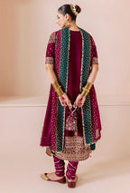 Woman in traditional maroon and green outfit with jewelry on a beige background