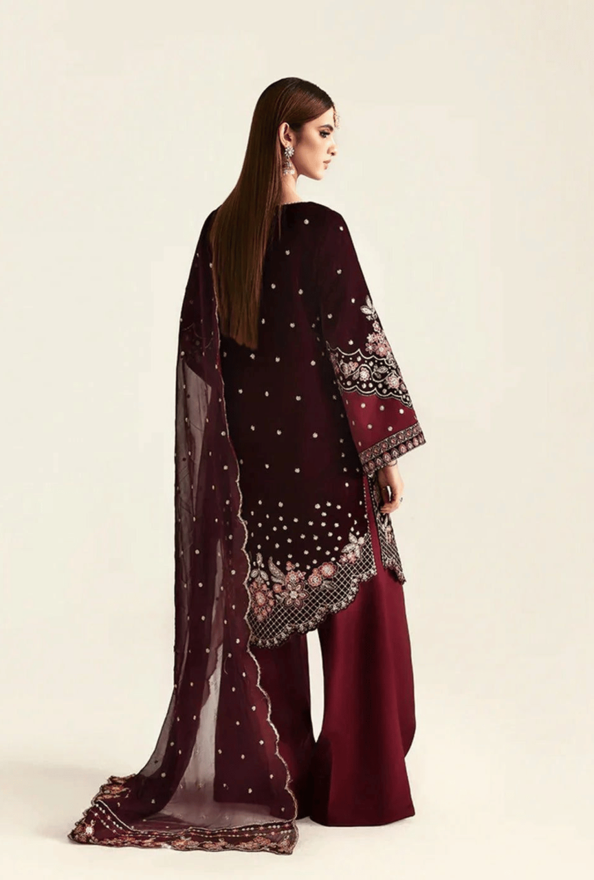 Woman wearing a burgundy embroidered outfit with a sheer dupatta on a beige background