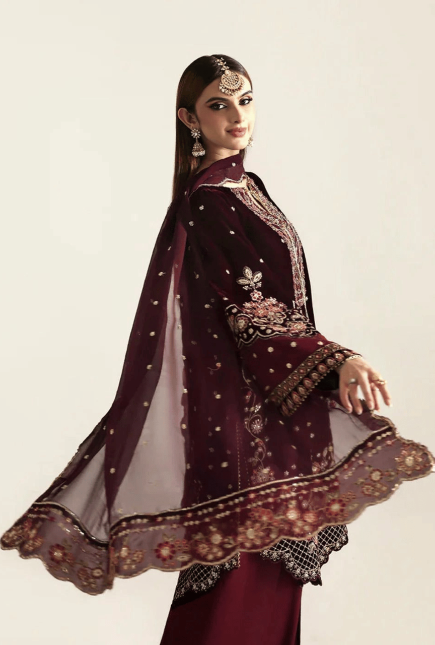 Woman wearing a maroon embroidered traditional outfit with a sheer dupatta on a beige background
