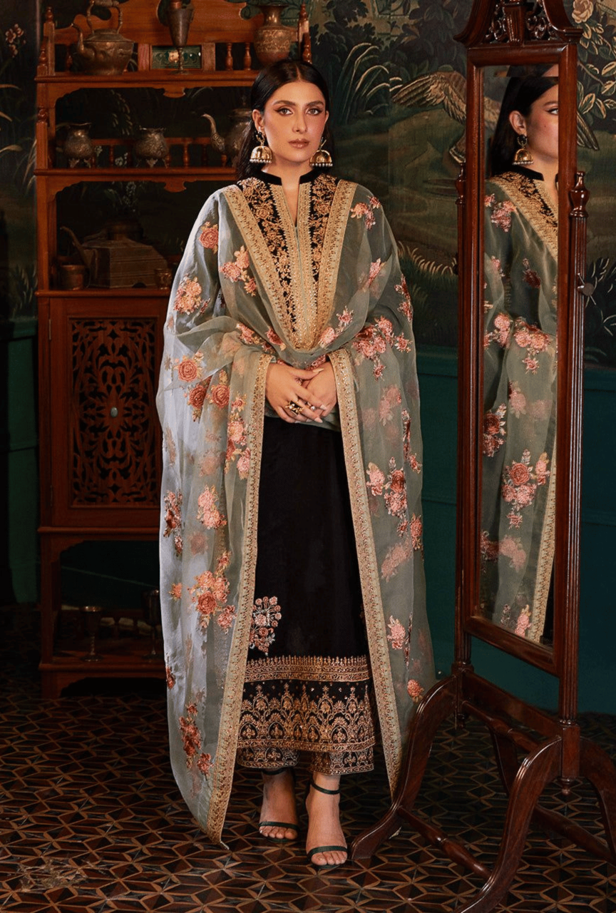 Woman in a floral embroidered outfit standing in front of a mirror with a decorative background.