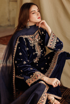 Woman wearing a navy blue embroidered traditional outfit sitting on a patterned rug.