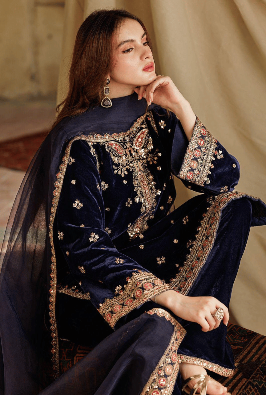 Woman wearing a navy blue embroidered traditional outfit sitting on a patterned rug.